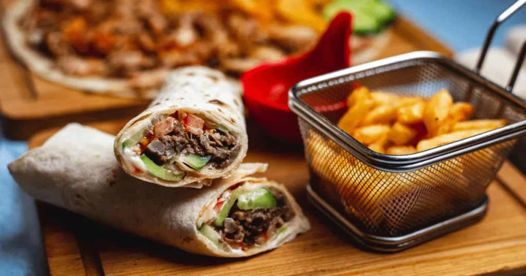 A delicious looking wrap shawarma filled with meat and vegetables, alongside a basket of crispy fries.